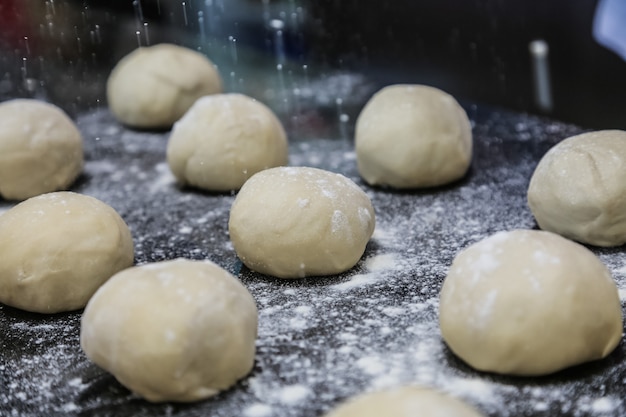 Flour pouring on formed dough bolls on black board side view