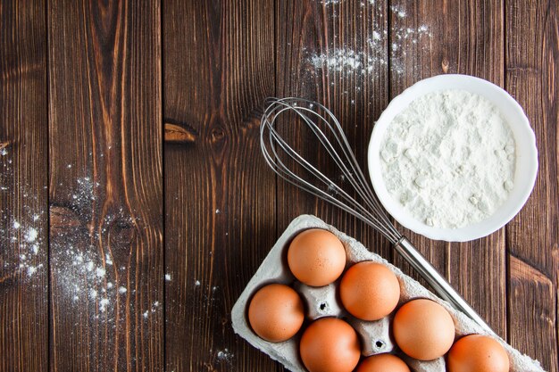 Flour with eggs, whisk in a bowl on wooden table, flat lay.