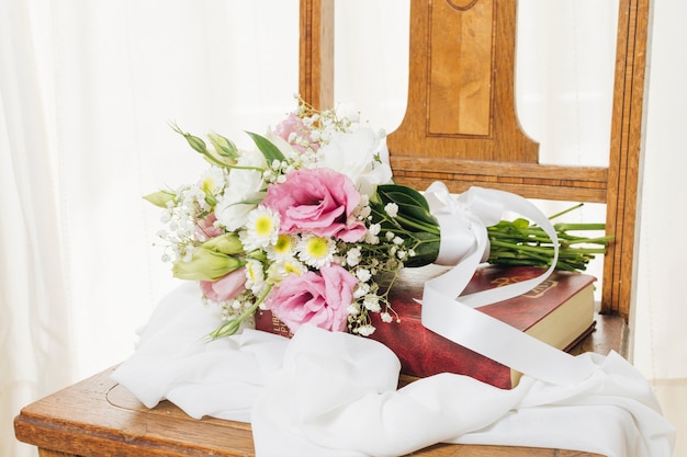 Free photo flower bouquet on book with scarf on wooden chair