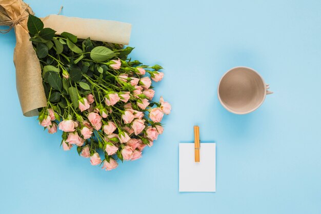 Flower bouquet; card and empty cup on blue background