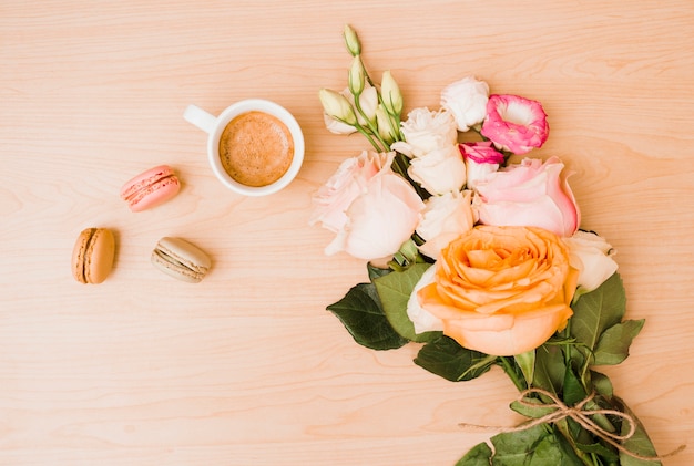 Free photo flower bouquet with coffee cup and macaroons on wooden desk