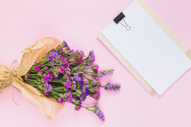 Flower bouquet wrapped in brown paper near the white blank paper on clipboard