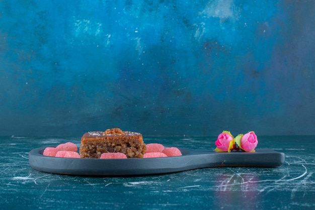 Free Photo flower corollas next to marmelades around a slice of bakhlava on a small serving pan on blue background. high quality photo