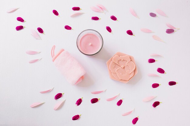 Flower petals around the rolled up soft napkin; candle and soap on white background