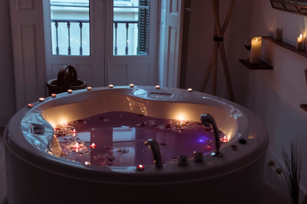 Free photo flower petals on water in spa tub with burning candles on edges