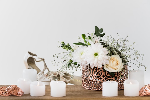 Free photo flower vase near the burning candle and wedding shoes against white background