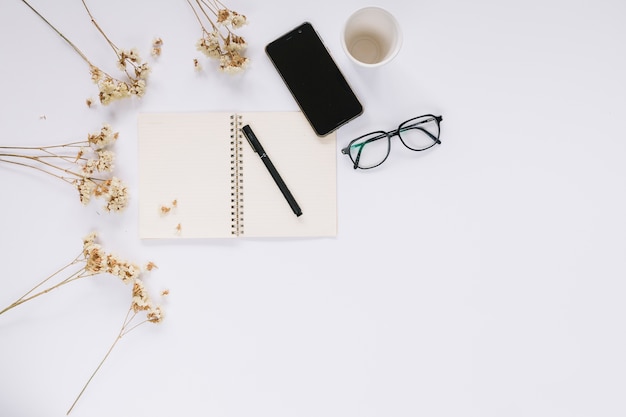 Free Photo flowers; cellphone; open notebook and eyeglasses on white desk