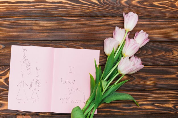 Flowers and child drawing with text I love you mom on wood table