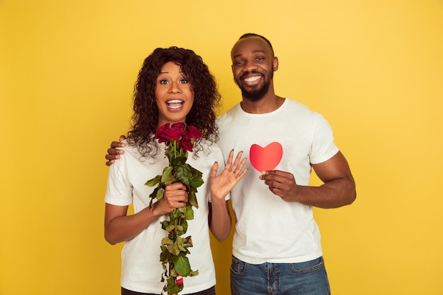 Free photo flowers and heart. valentine's day celebration, happy african-american couple isolated on yellow studio background.