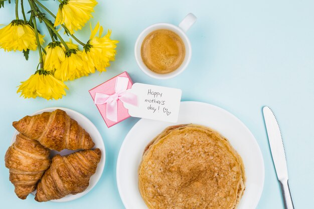 Flowers near present with tag and plates with crepes and croissants