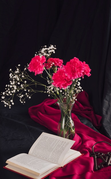 Free photo flowers with bloom twigs in vase near volume and keys on pink textile in darkness