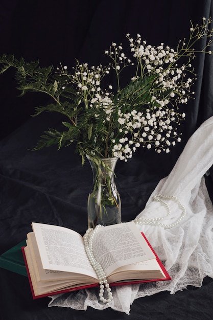 Free photo flowers with plants in vase near volume and beads on white textile