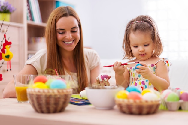 Focus little girl painting easter eggs with her mother