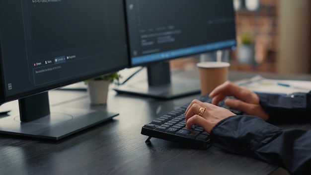 Free photo focus on software developer hands typing source code on keyboard while looking at computer screens with programming interface. programer sitting at desk with clipboard writing algorithm.