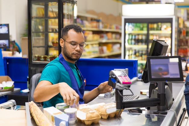 Focused African American cashier scanning goods at checkout