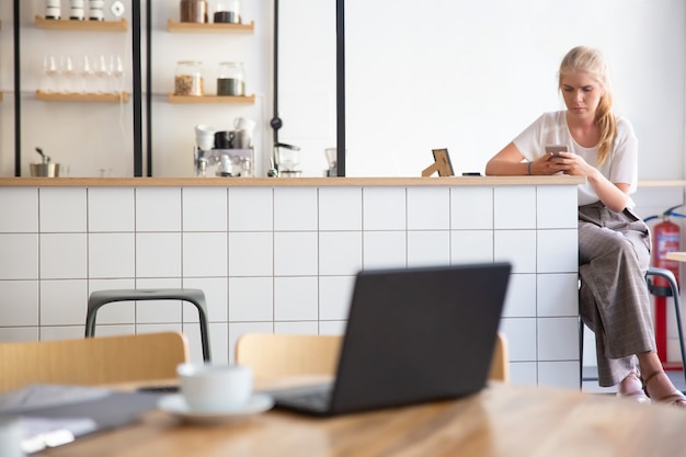 Free Photo focused beautiful blonde woman using smartphone, sitting at kitchen counter in co-working space