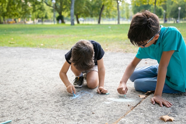 Focused boys sitting and drawing with colorful chalks. Childhood and creativity concept