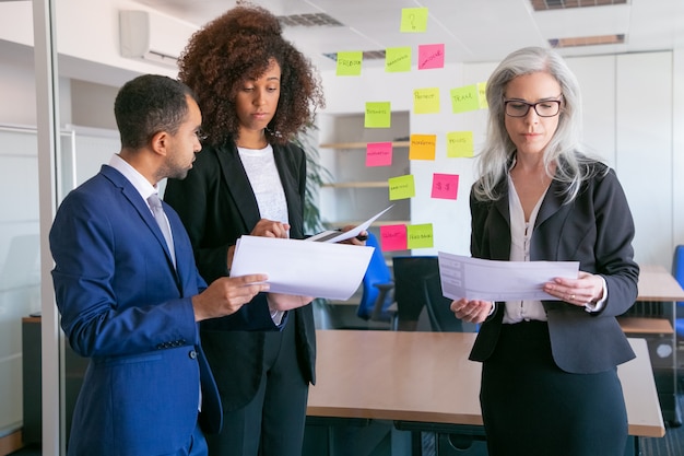 Focused businesspeople reading documents with statistics. Successful concentrated office employers in suits meeting in office room and studying reports. Teamwork, business and management concept