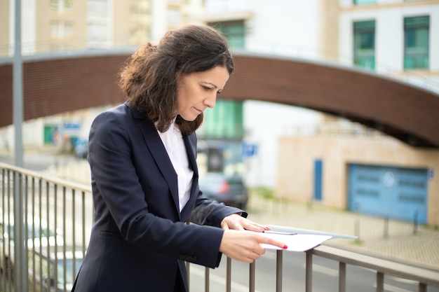 Focused businesswoman reading papers on street