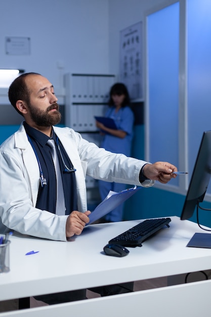 Focused doctor pointing at computer for analysis work at night