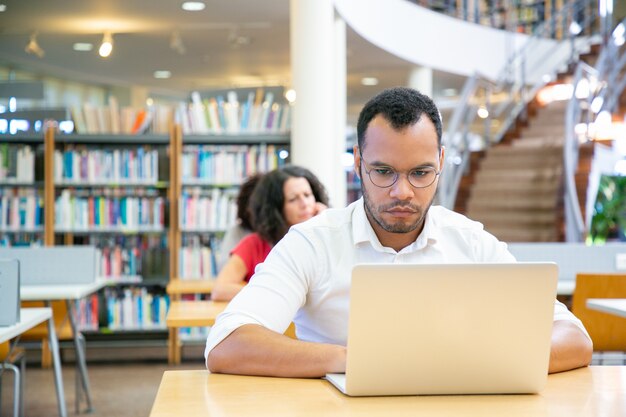 Focused male adult student doing research in library