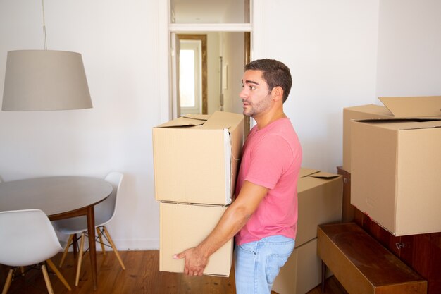 Focused man carrying carton boxes into new apartment, moving into new flat