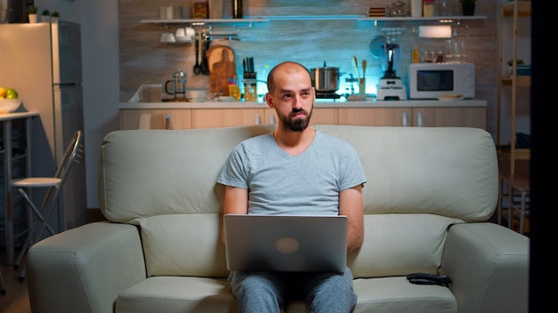 Free Photo focused man sitting on sofa and writing online project on laptop