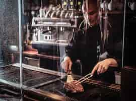 Free photo focused master chef cooking delicious beef steak on a kitchen, standing behind protective glass in a restaurant.