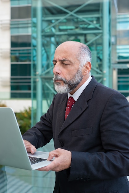 Free photo focused mature businessman with laptop checking email