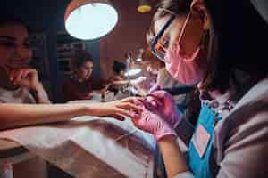 Free photo focused talented manicurist is working at her own workplace at busy beauty salon. she is wearing protective mask.