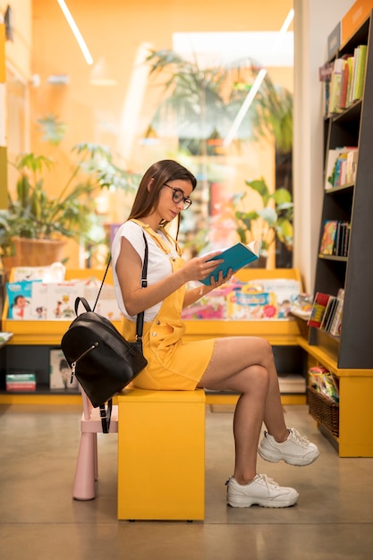 Focused teen schoolgirl reading book on seat