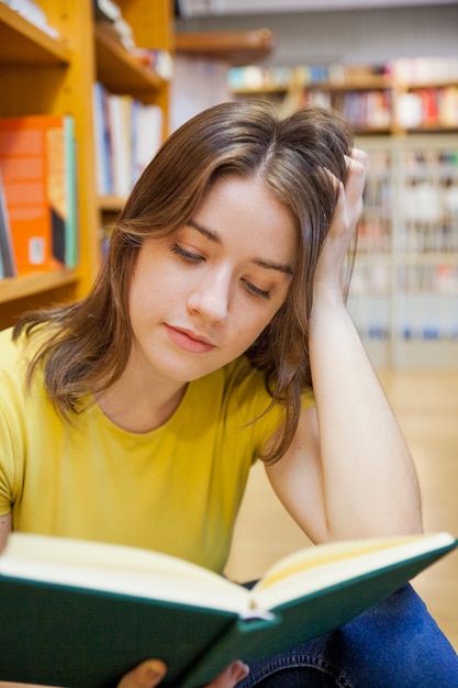 Focused teenager reading near bookcase