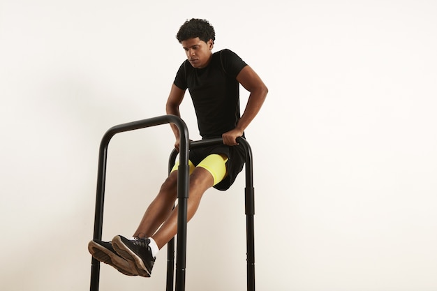 Free photo focused young african american athlete in black sportswear performing bodyweight rows on mobile bars isolated on white