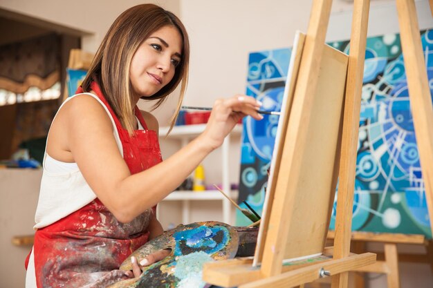 Focused young female artist working on a new painting in her workshop