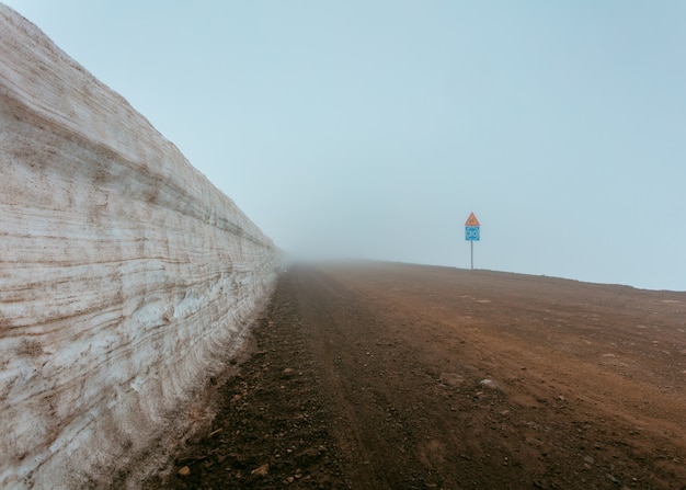 A foggy muddy road next to a wall and road signs