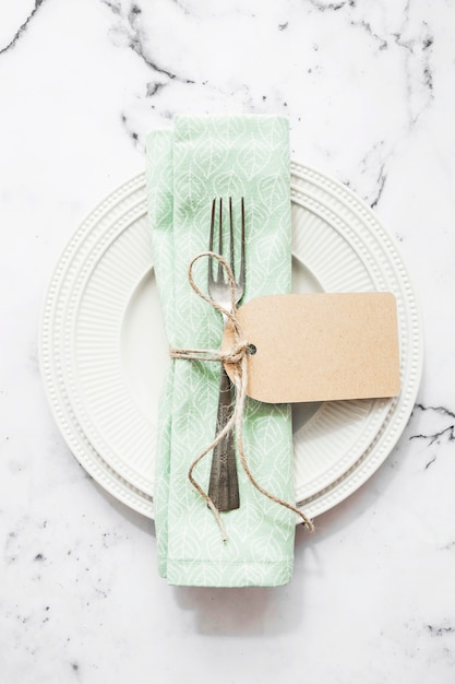 Free Photo folded napkin and fork tied with string and blank tag on white ceramic plate