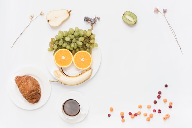 Free photo food arranged as human face on plate with coffee; croissant and coffee on white background