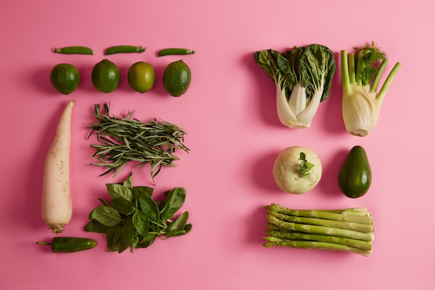 Food and fresh vegetables. Green asparagus, lime, avocado, white radish, rosemay, basil isolated on pink surface. Products or ingredients for making organic healthy meals. Dieting, agriculture