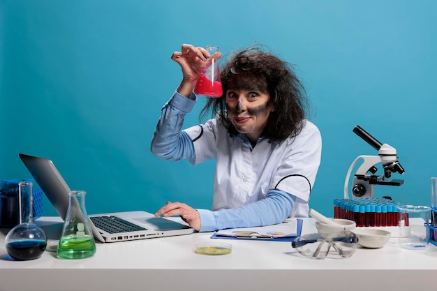 Foolish funny looking crazy chemist having glass flask filled with experimental liquid serum after failed chemical experiment. Mad silly lab worker having wild look and weird face expression.