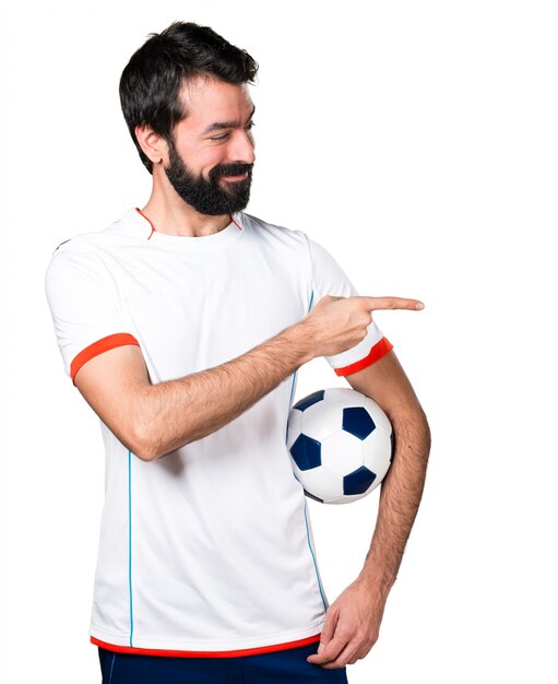 Football player holding a soccer ball pointing to the lateral