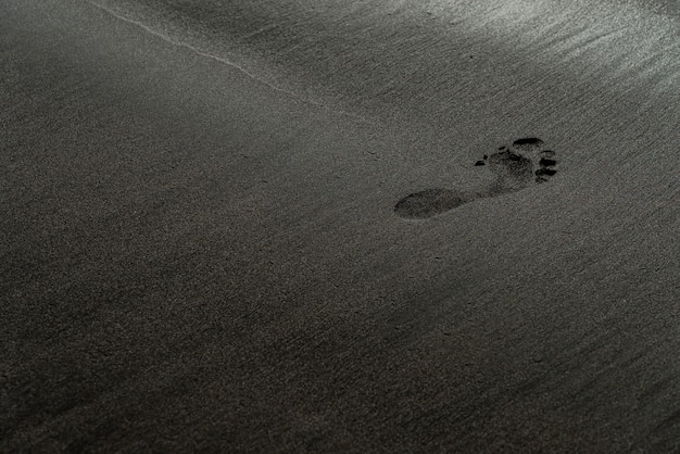 Free Photo footprint on a black sand beach macro photography. human trace on a silky black beach texture with shallow depth of field. minimalistic black background. tenerife voulcanic sandy shore.