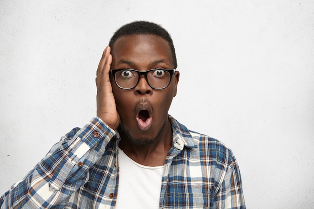 Forgetful Afro-American student in stylish glasses holding hand on head staring with astonished amazed look, having completely forgotten about serious examination at college.