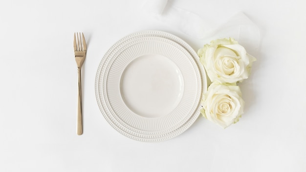 Fork; ceramic plate; roses and satin ribbon on white background