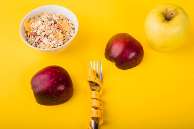 Free photo fork in measuring tape between apples and bowl of muesli