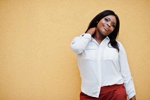 Formally dressed african american business woman in white blouse and red trousers isolated on yellow background Successful dark skinned businesswoman