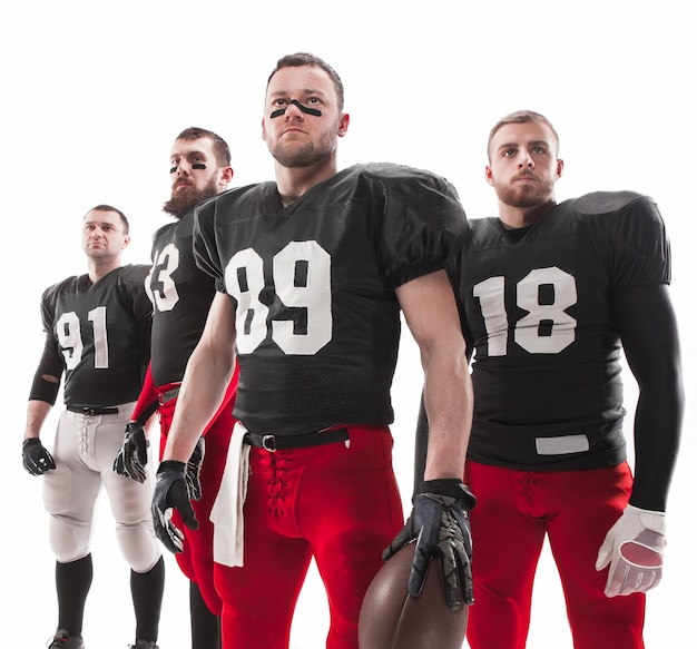 Free photo the four caucasian fitness men as american football players posing  full-length with a ball on white background