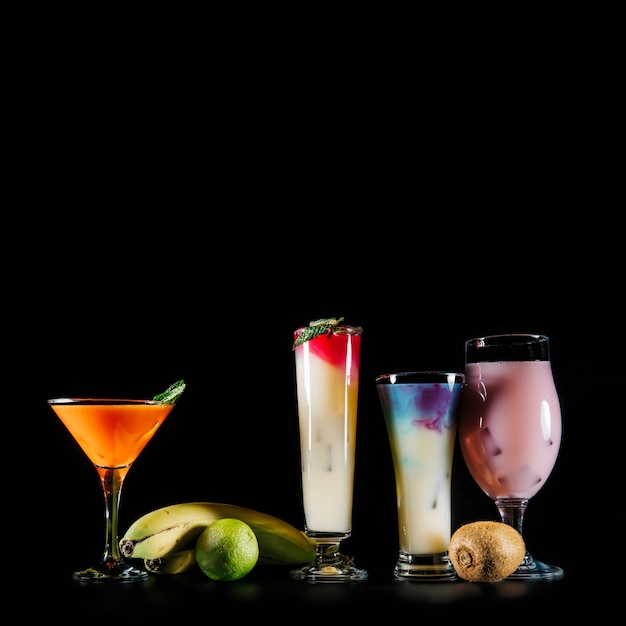 Free photo four cocktails and exotic fruits on black background