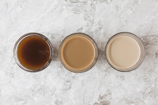 Four coffee cups in a row on marble backdrop displaying different mixtures of milk and coffee