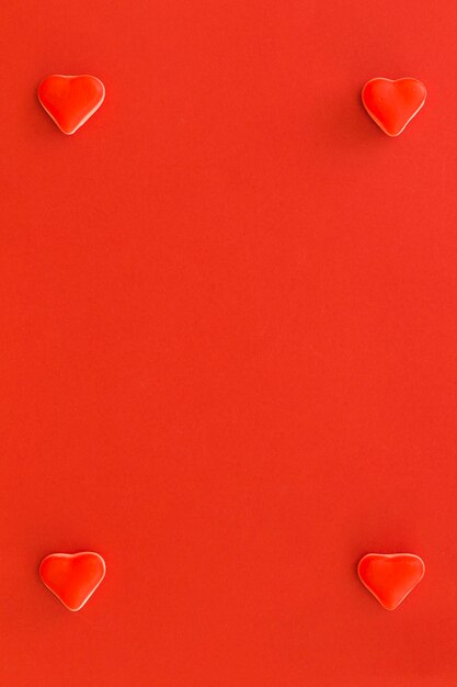 Four heart shape candies at the corner of red background