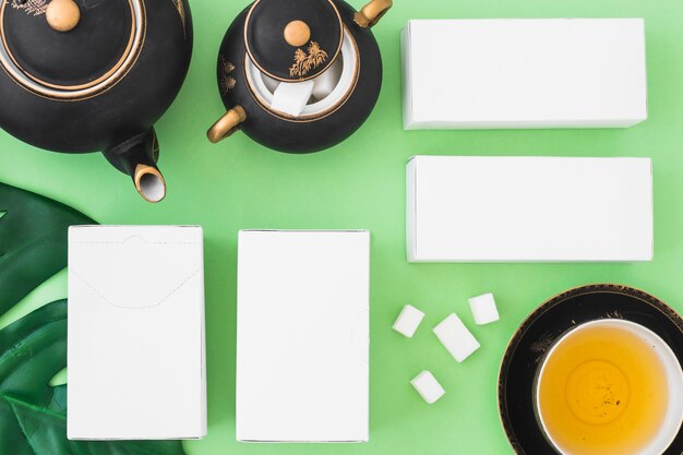 Four white boxes with herbal tea and sugar cubes on green backdrop